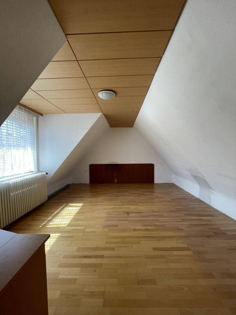 Helles Dachzimmer mit Holzboden, schrägen Wänden und Holzdeckenverkleidung.