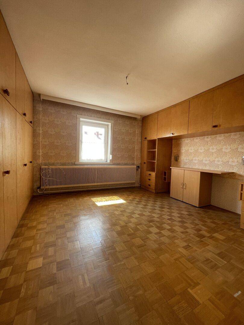 Schlafzimmer mit Parkettboden, eingebauten Holzschränken und einem Fenster mit Tageslicht.