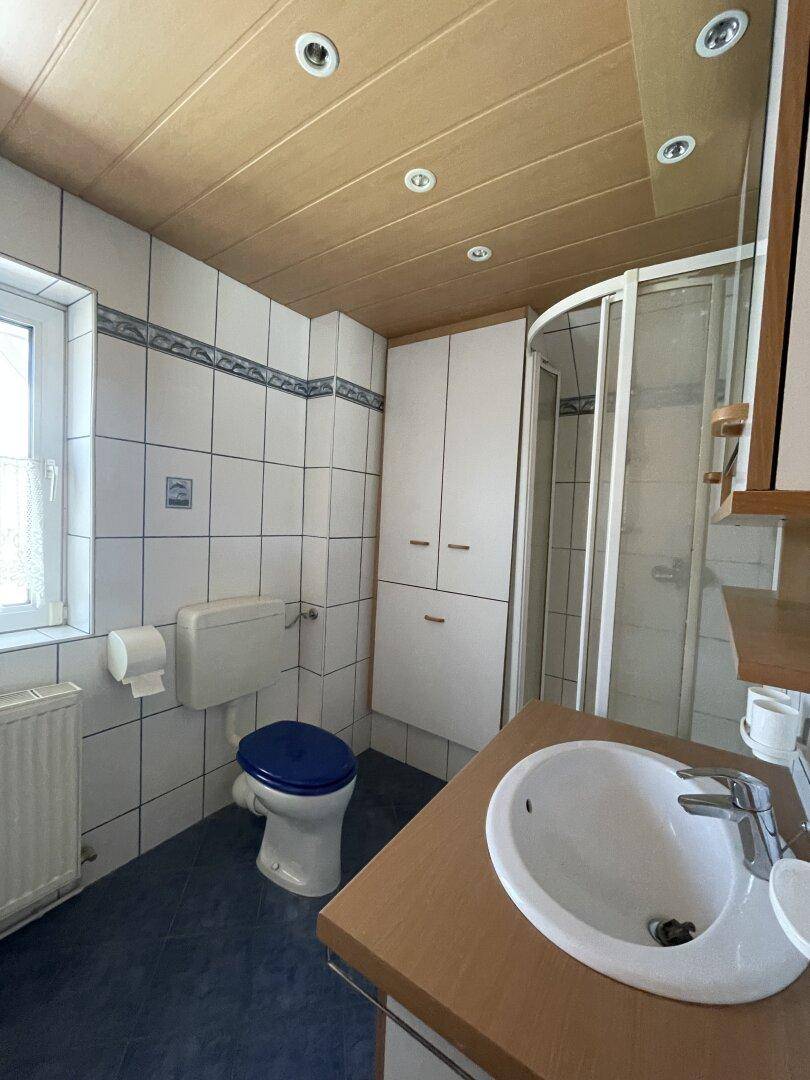 Badezimmer mit Duschkabine, WC, Waschbecken und einem Fenster, alles in hellen Fliesen gehalten.