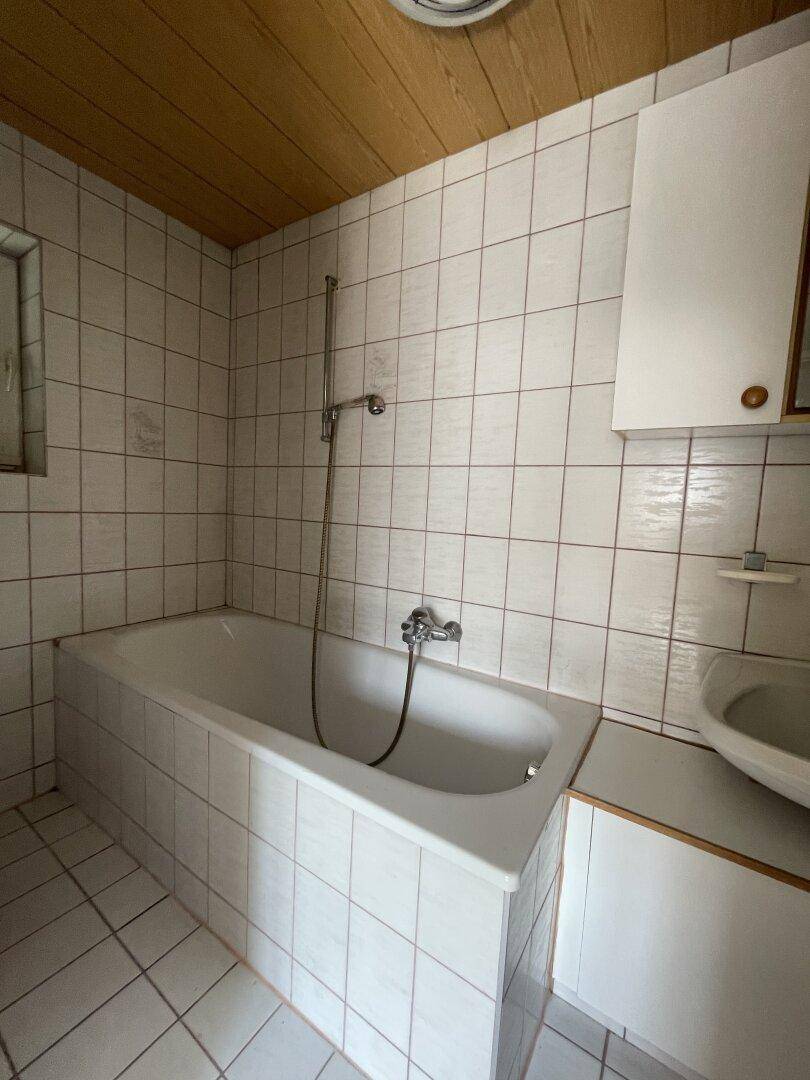 Badezimmer mit Badewanne, Waschbecken und weißen Fliesen, ergänzt durch eine Holzdecke.