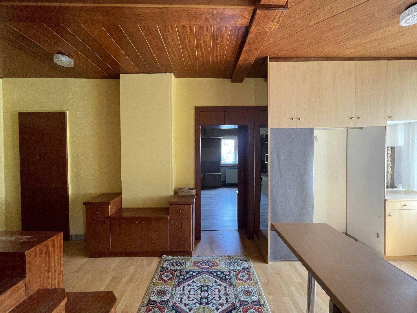 Wohnzimmer mit Holzbalkendecke, Parkettboden und traditionellem Teppich sowie Einbaumöbeln.