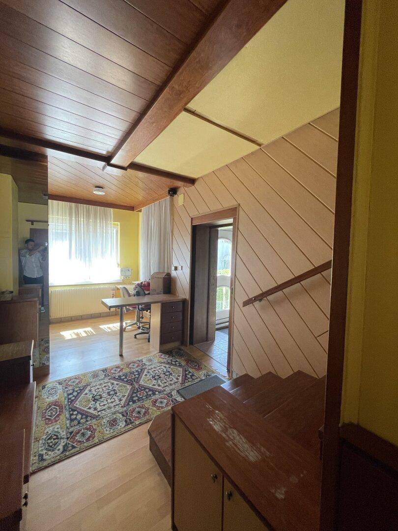 Flur mit Holztreppe, Holzvertäfelung an der Wand und einem Fenster, das Tageslicht hereinlässt.