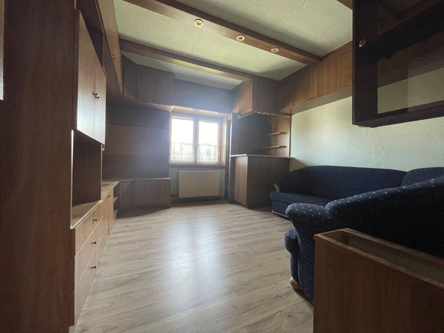 Gemütliches Wohnzimmer mit Holzvertäfelung, Einbauschränken und Blick ins Grüne durch das Fenster.