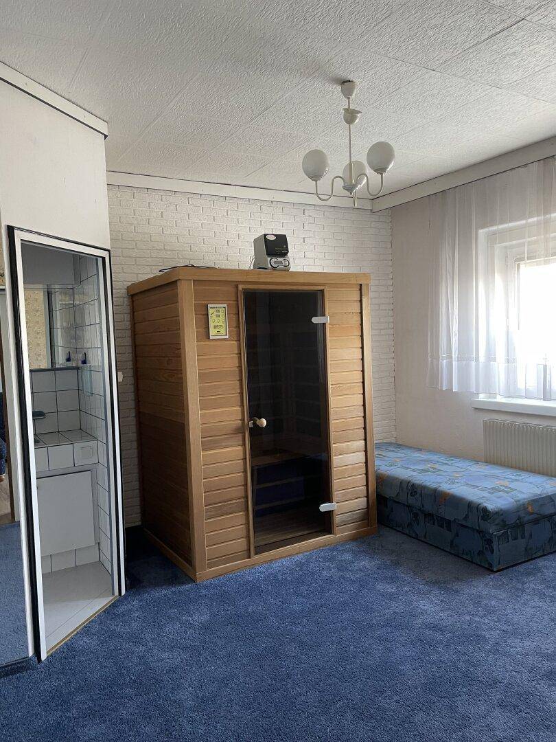 Schlafzimmer mit integrierter Sauna, blauer Teppichboden und Fenster für natürliches Licht.