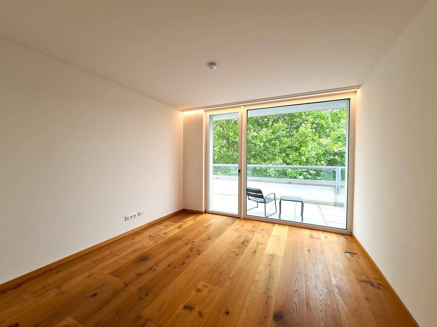 Heller Raum mit Holzboden und großen Schiebetüren, die zu einem Balkon führen.