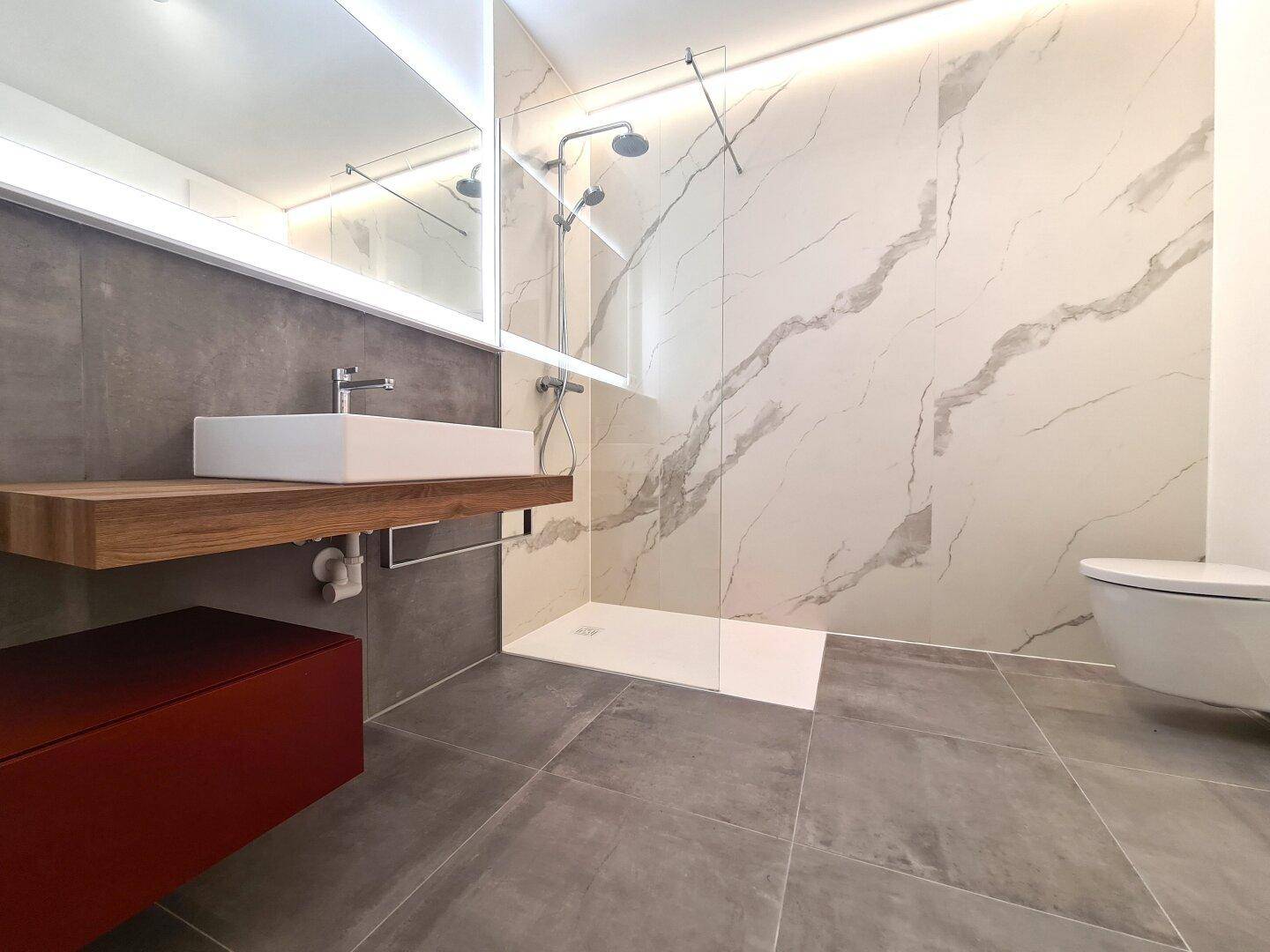 Modernes Badezimmer mit schwebendem Holzwaschtisch, begehbarer Dusche und eleganten Marmor-Effekt-Fliesen.