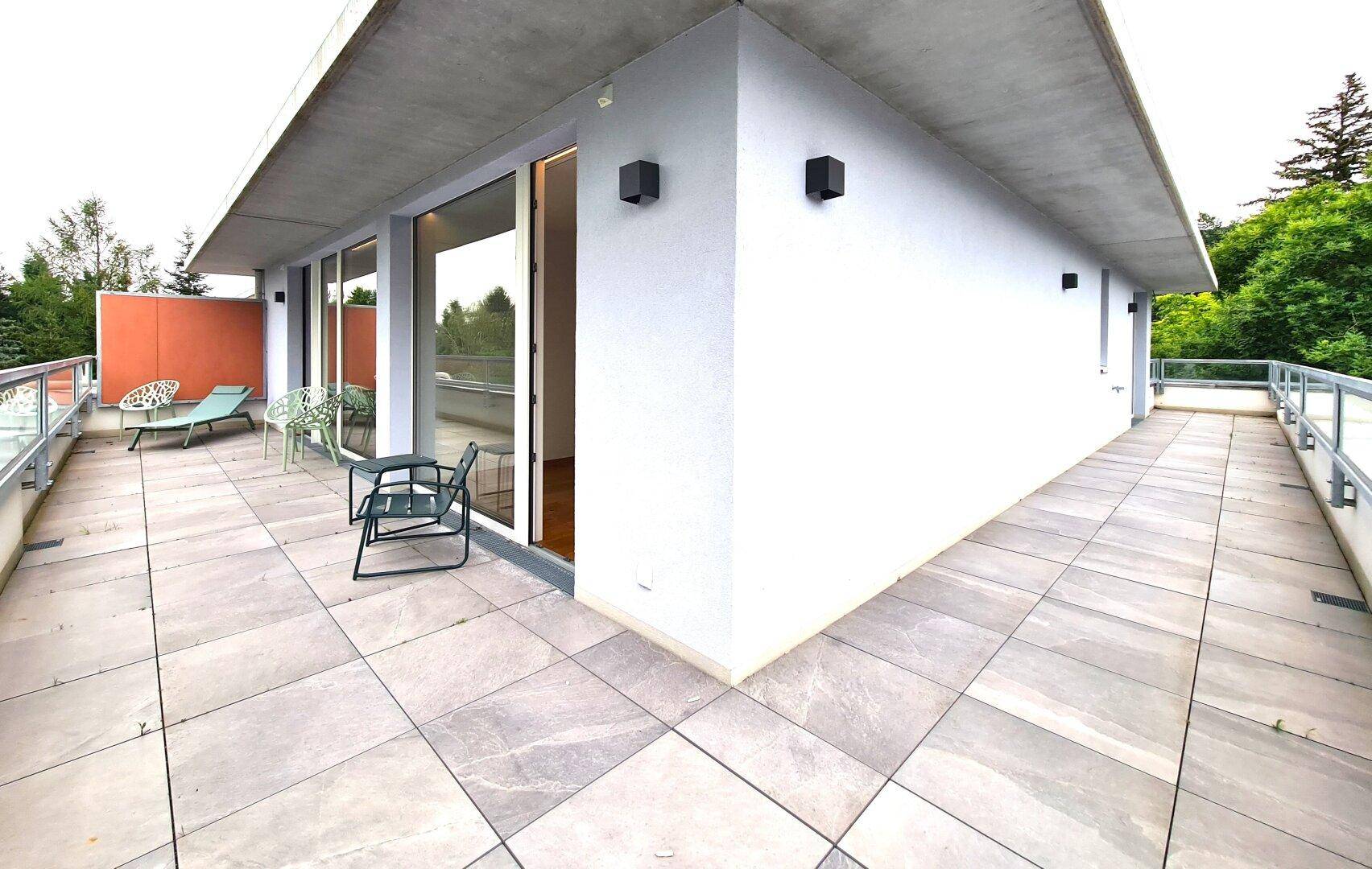 Große Dachterrasse mit Fliesenboden und Sitzgelegenheiten, umgeben von Bäumen.