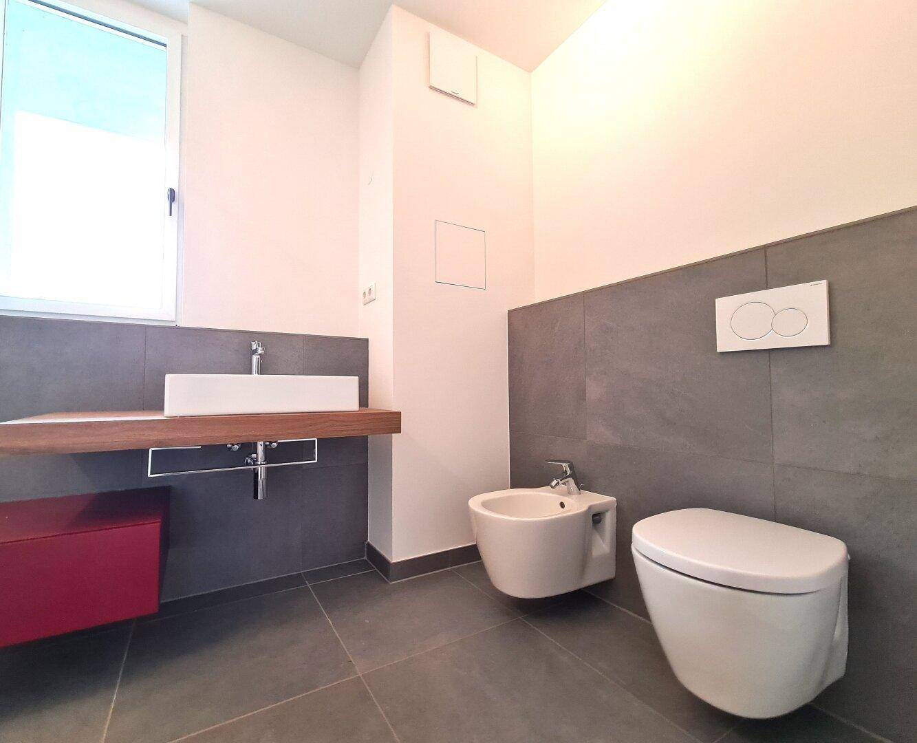 Modernes Badezimmer mit Waschtisch, Bidet und wandhängendem WC, ausgestattet mit Fenster.