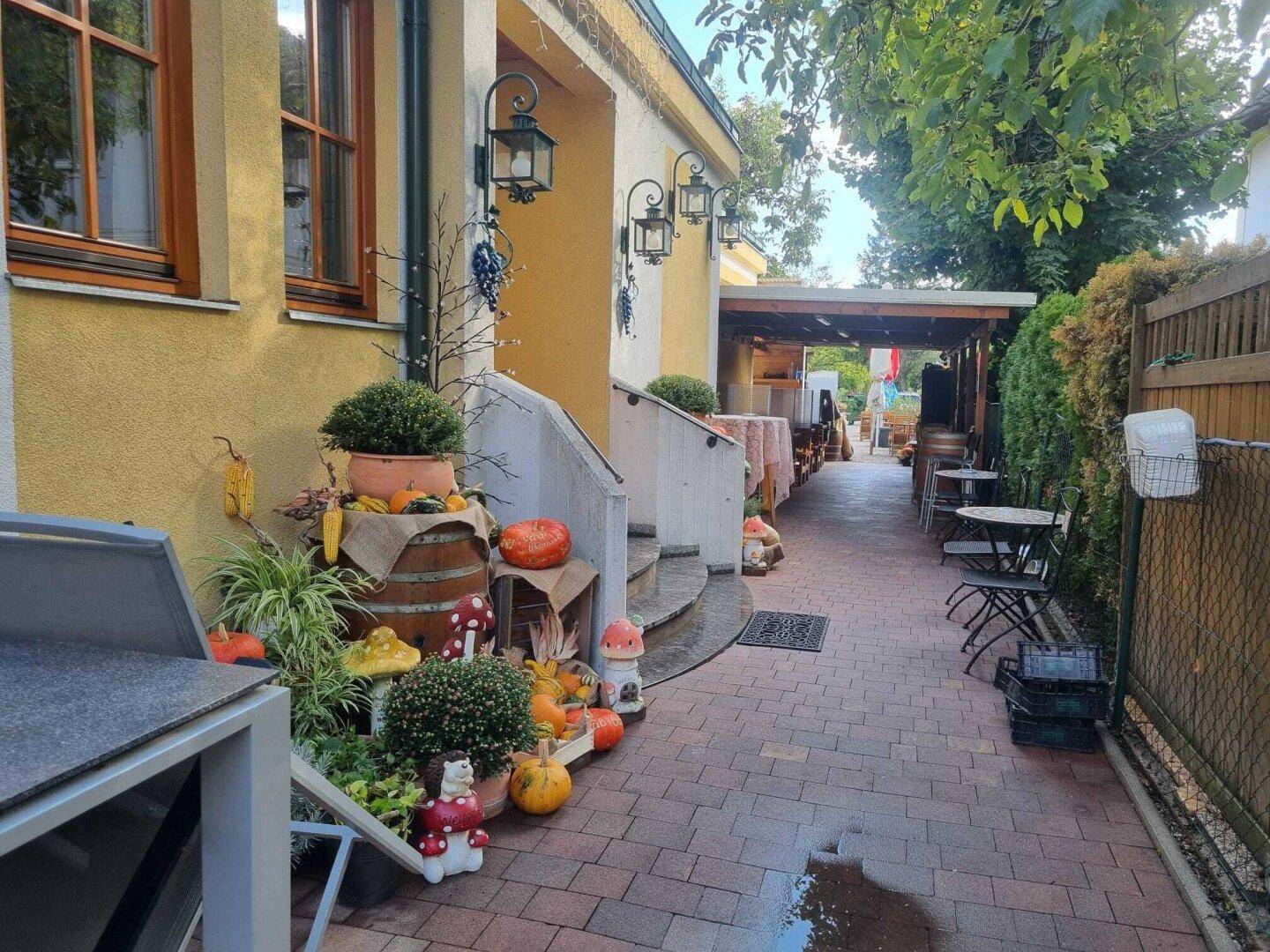 Seitlicher Eingangsbereich mit herbstlicher Dekoration, gepflastertem Weg und Außenbeleuchtung.