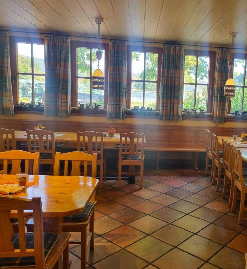 Heller Restaurantbereich mit mehreren Fenstern, Holztischen und traditionellen Vorhängen.