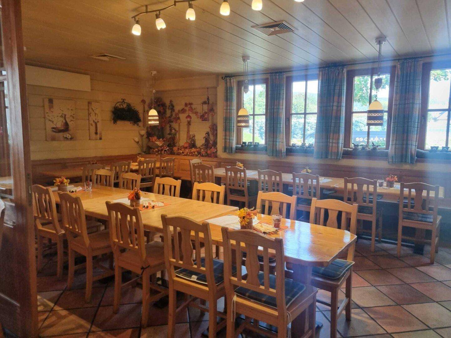Geräumiger Restaurantbereich mit Holztischen, Bänken und großen Fenstern, die viel Licht hereinlassen.