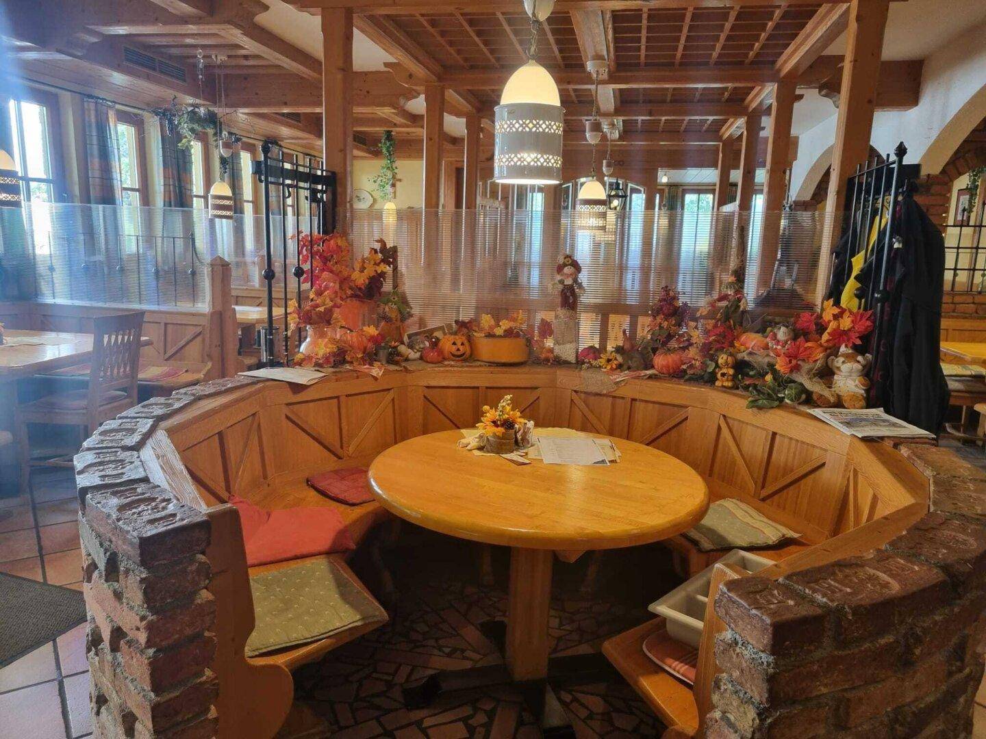 Gemütliche Sitzecke im Restaurant mit runden Holztischen, Bänken und herbstlicher Dekoration.