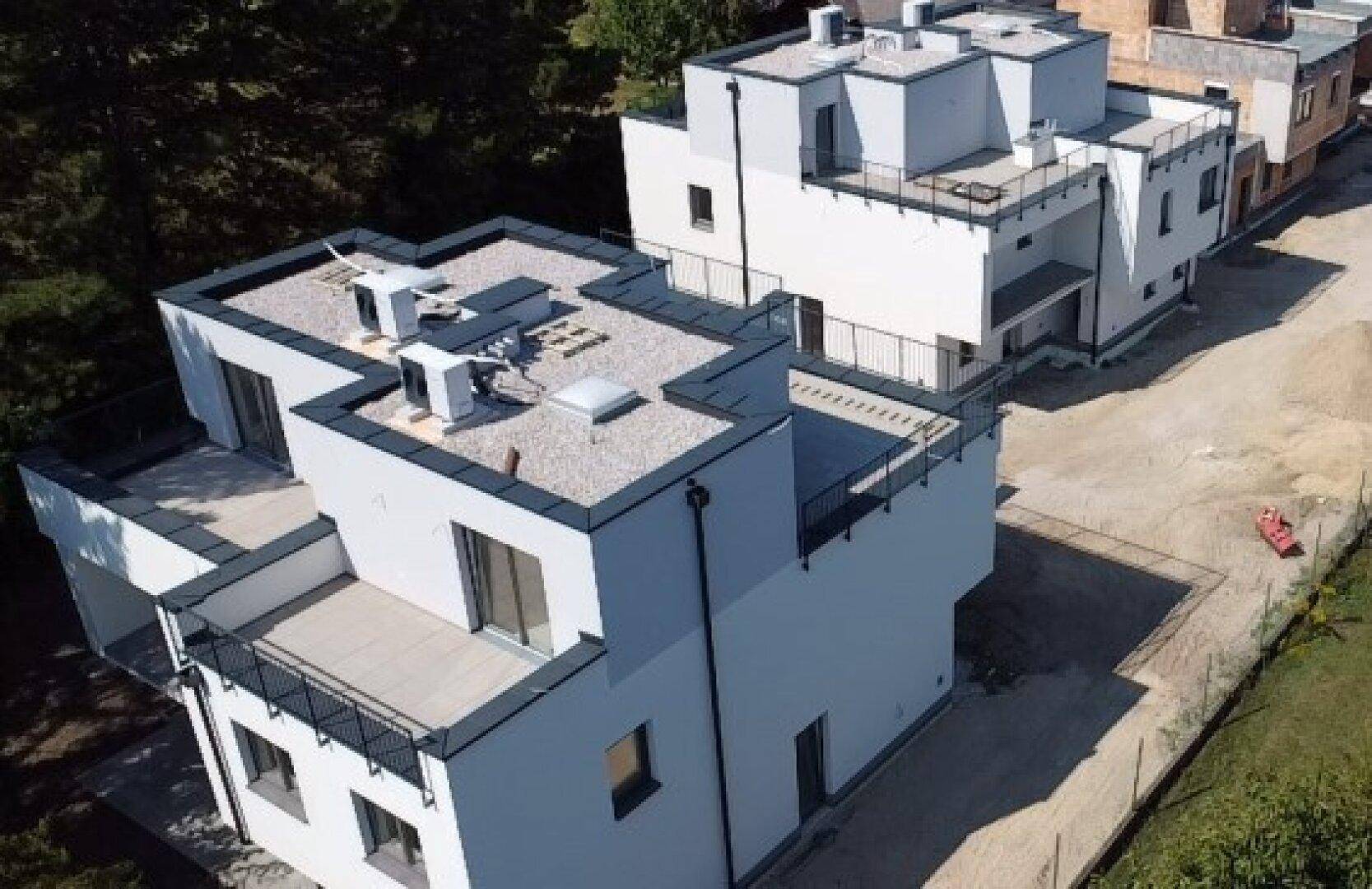 Moderne Reihenhäuser mit Flachdach, Balkonen und Terrassen im Bauzustand, umgeben von Grün.