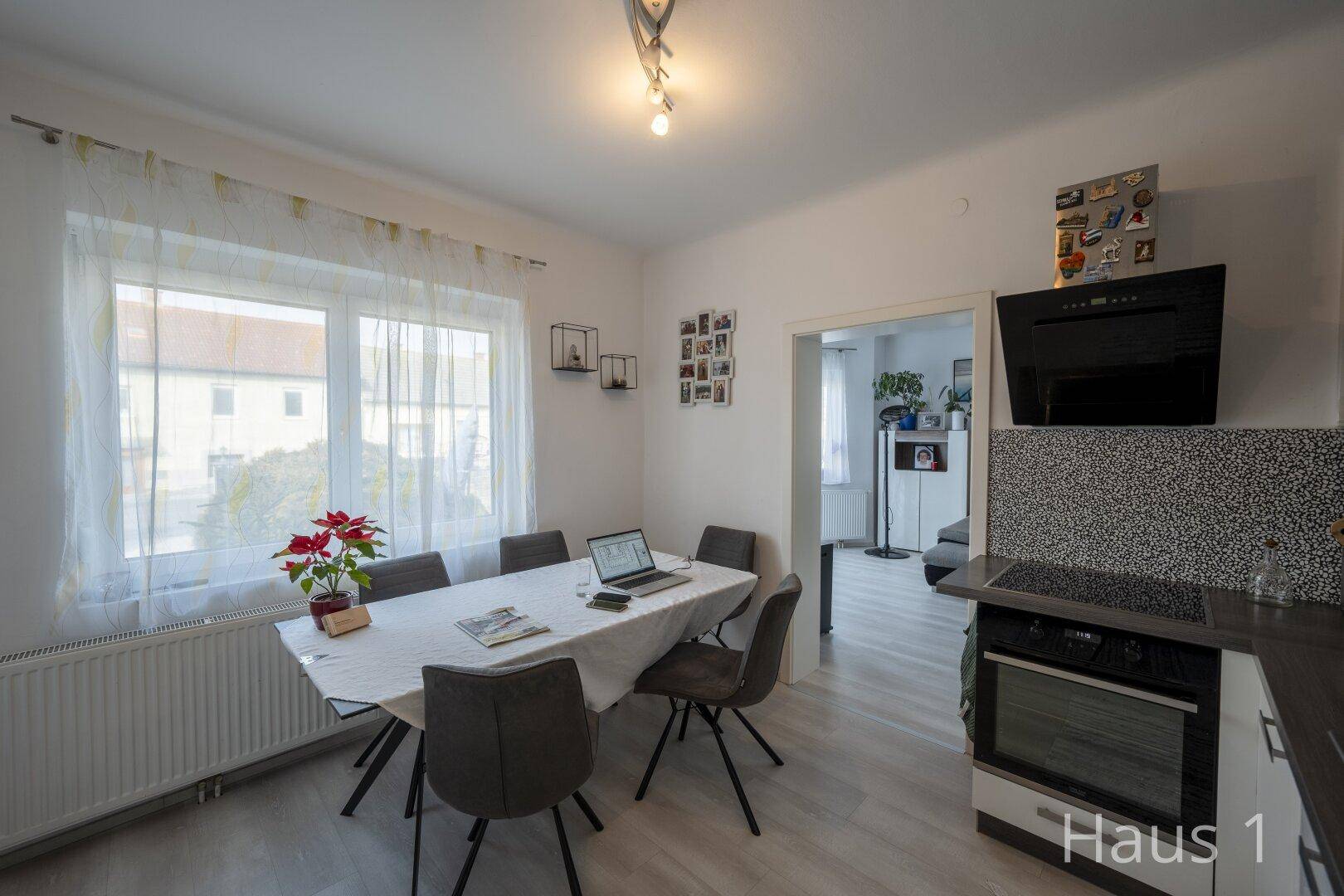 Helle Küche mit Essbereich, modernen Geräten und Blick nach draußen durch große Fenster.