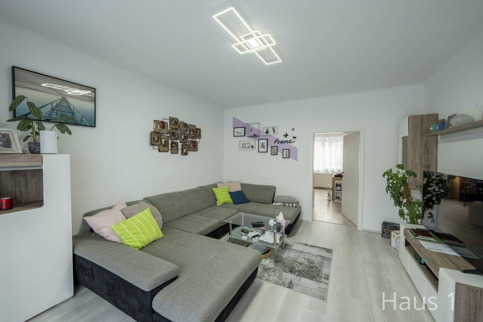 Gemütliches Wohnzimmer mit großem Ecksofa, modernem Lichtdesign und heller Einrichtung.