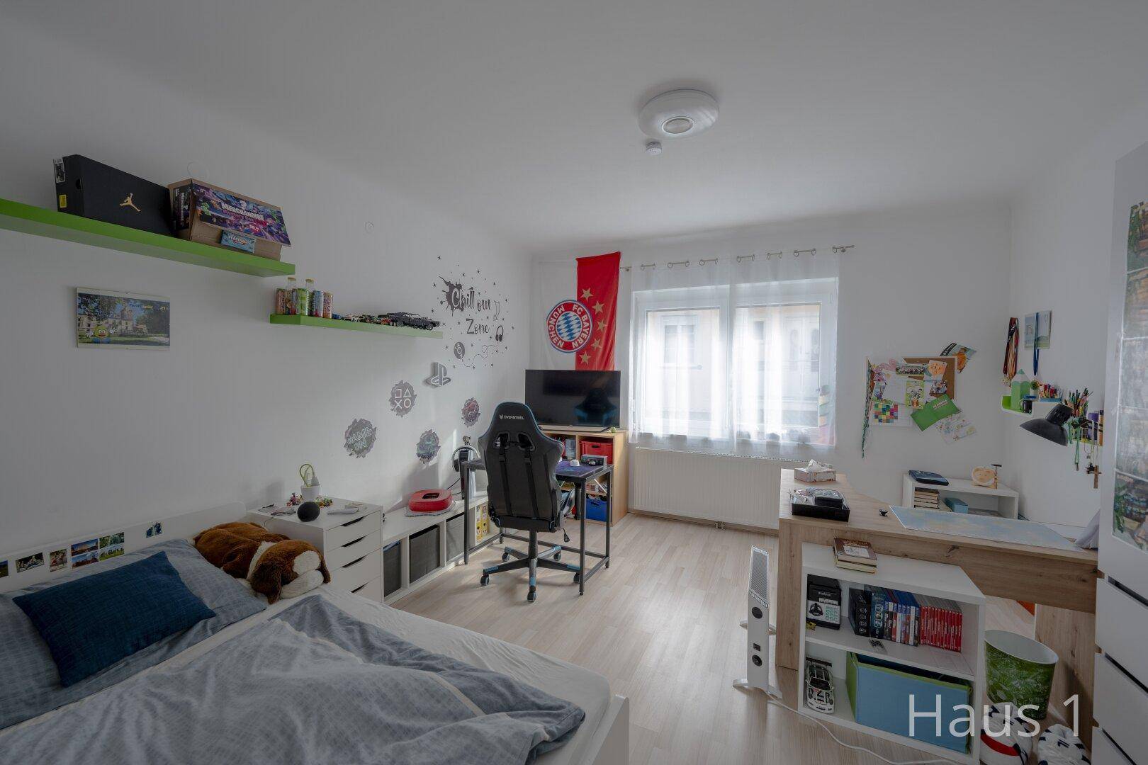 Jugendzimmer mit Bett, Schreibtisch und Regalen, hell und persönlich eingerichtet.