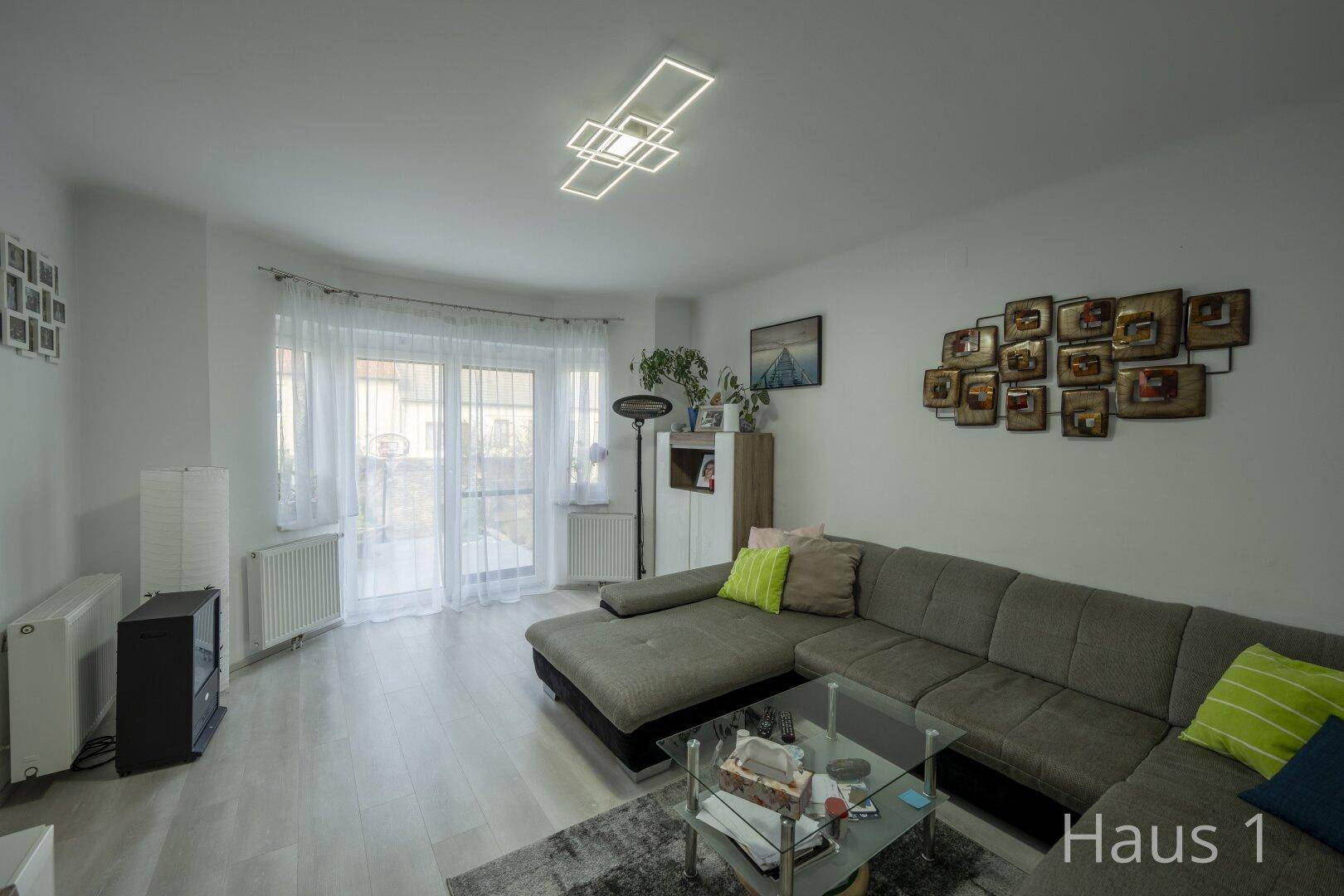 Helles Wohnzimmer mit großem Ecksofa, Zugang zum Balkon und moderner Dekoration.