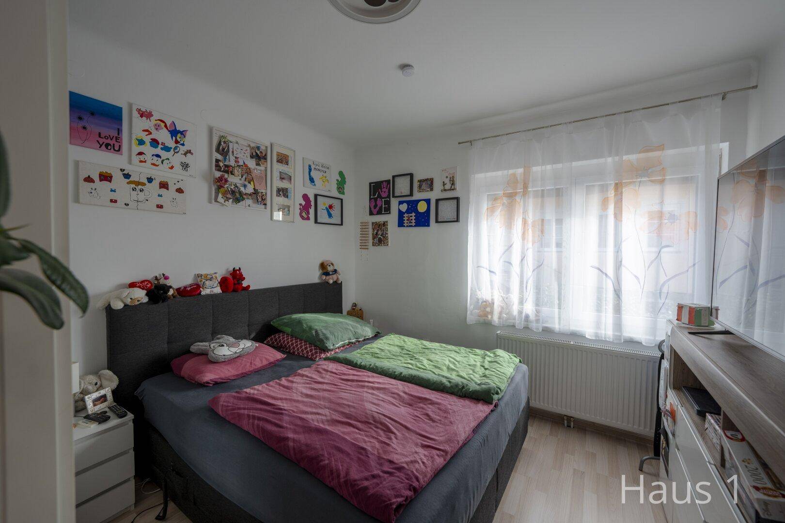 Schlafzimmer mit Doppelbett, Fenster und individueller Wanddekoration, hell und freundlich.
