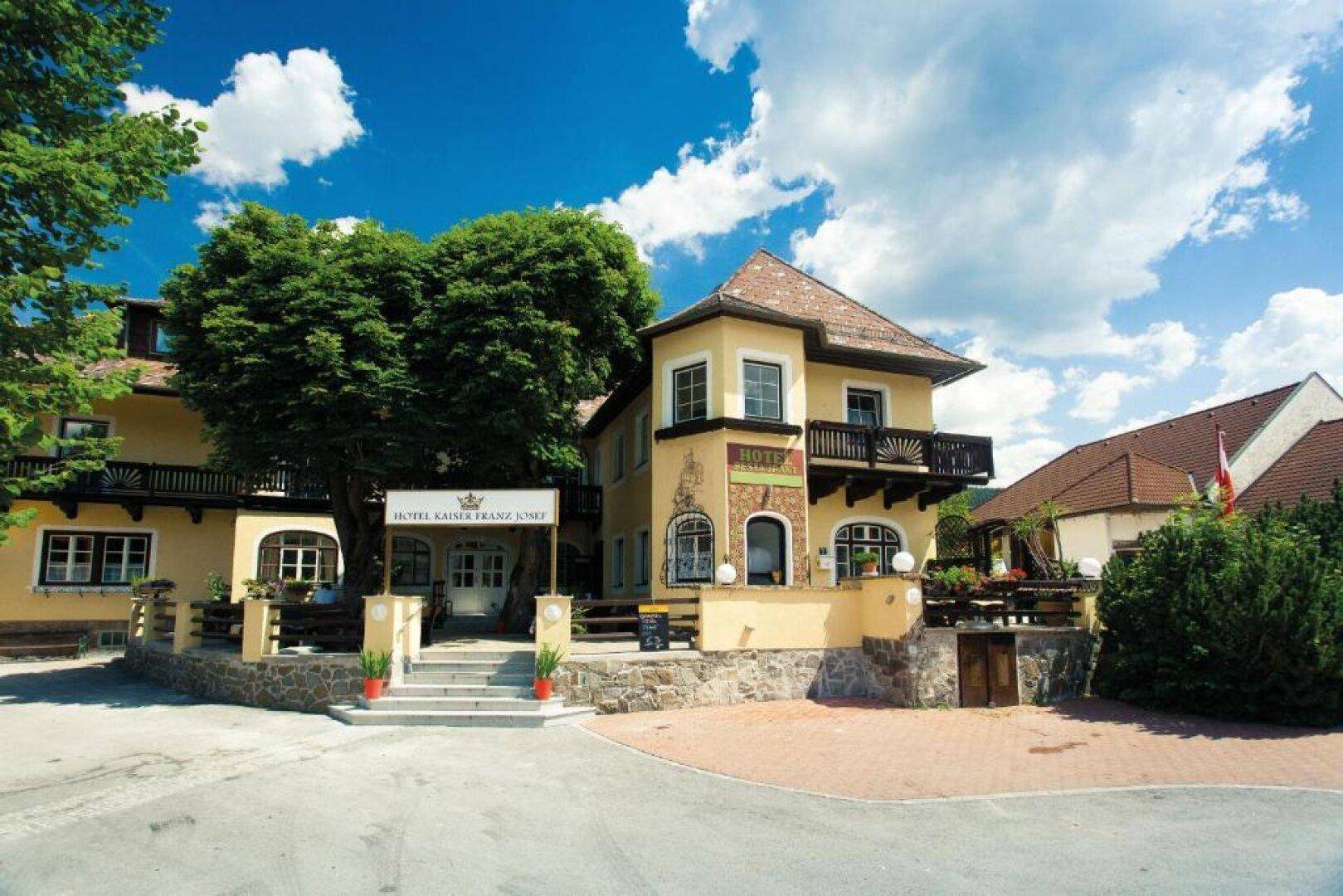 Traditionelles Hotelgebäude mit Balkonen und einem einladenden Eingangsbereich unter blauem Himmel.