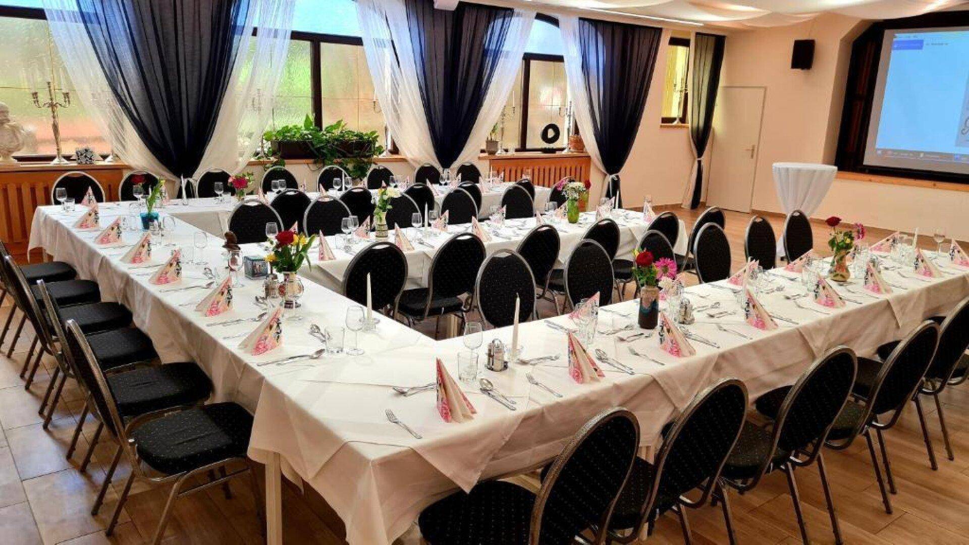 Großer Veranstaltungsraum mit U-förmiger Tischordnung, bereit für eine Feier oder Konferenz.