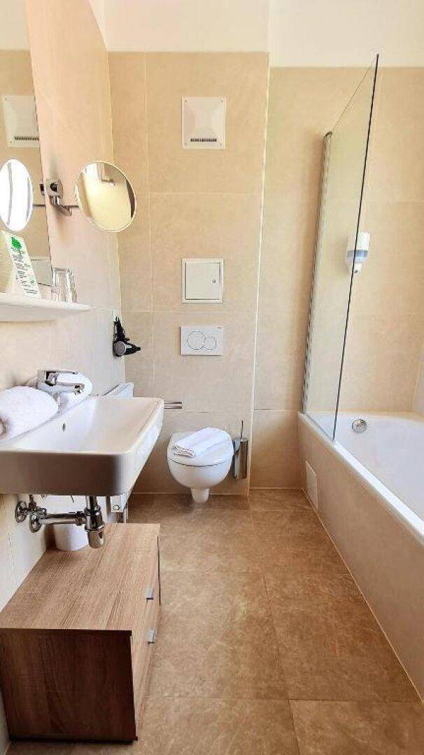 Helles Badezimmer mit Badewanne, WC und Waschbecken, ausgestattet mit beigen Fliesen.
