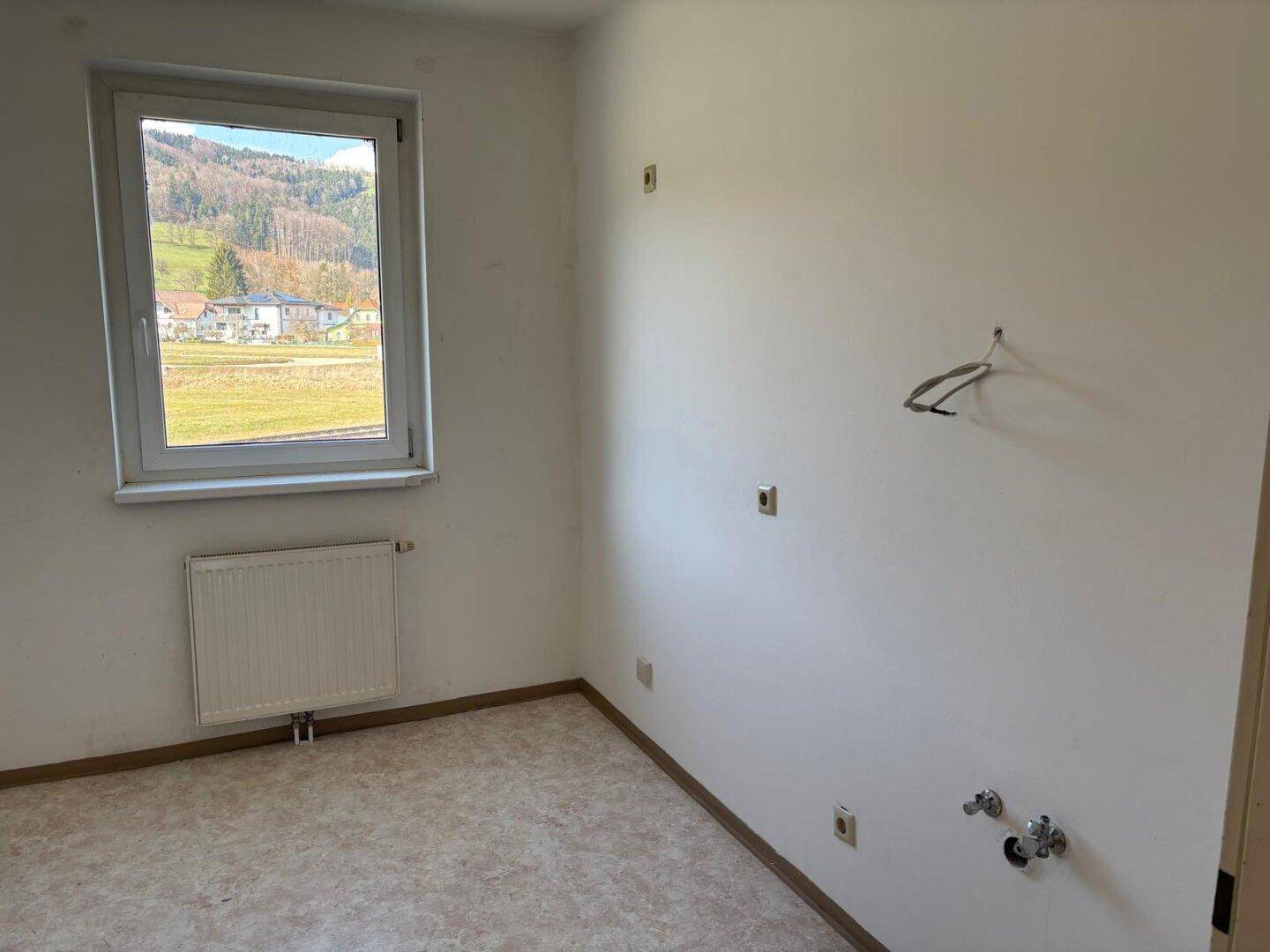 Leerer Raum mit PVC-Boden und sichtbaren Anschlüssen für Waschmaschine oder Spülbecken.