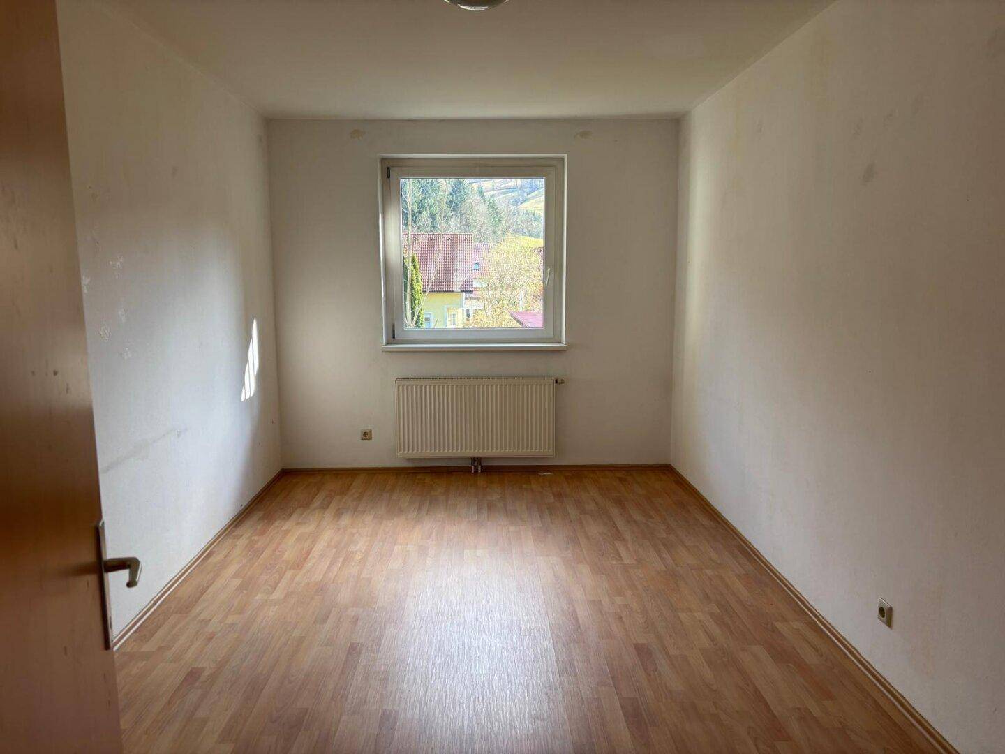Helles Zimmer mit Laminatboden und Fenster mit Blick auf die umliegende Natur.