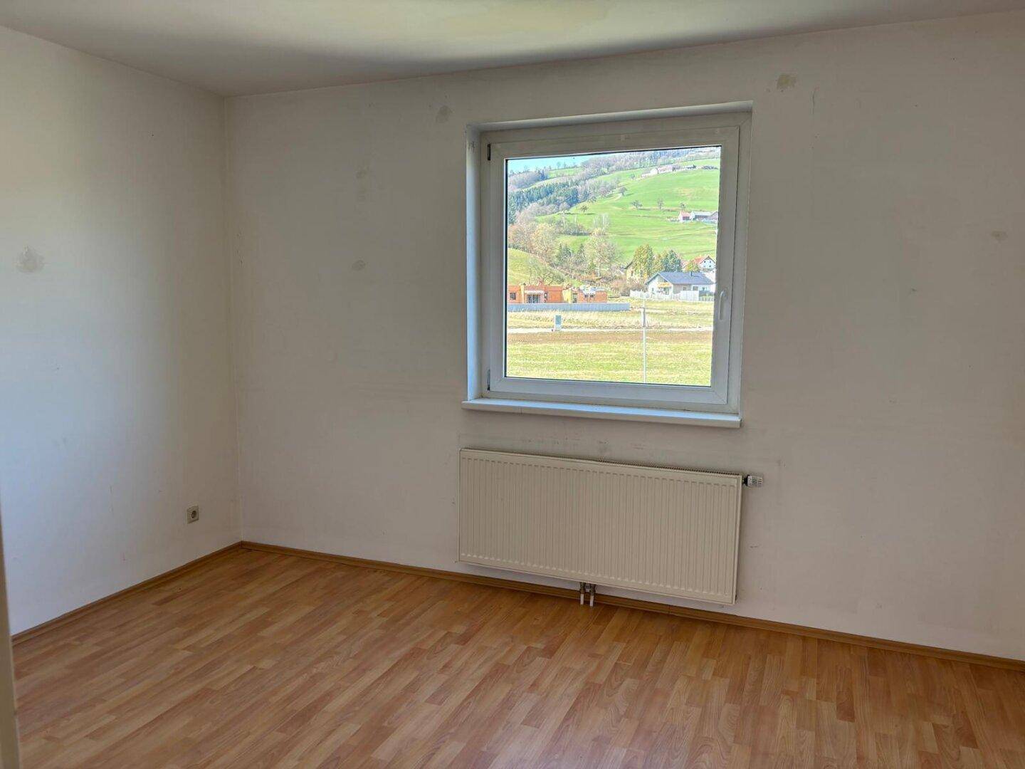 Zimmer mit Laminatboden, Heizkörper und weitem Blick auf die grüne Landschaft.