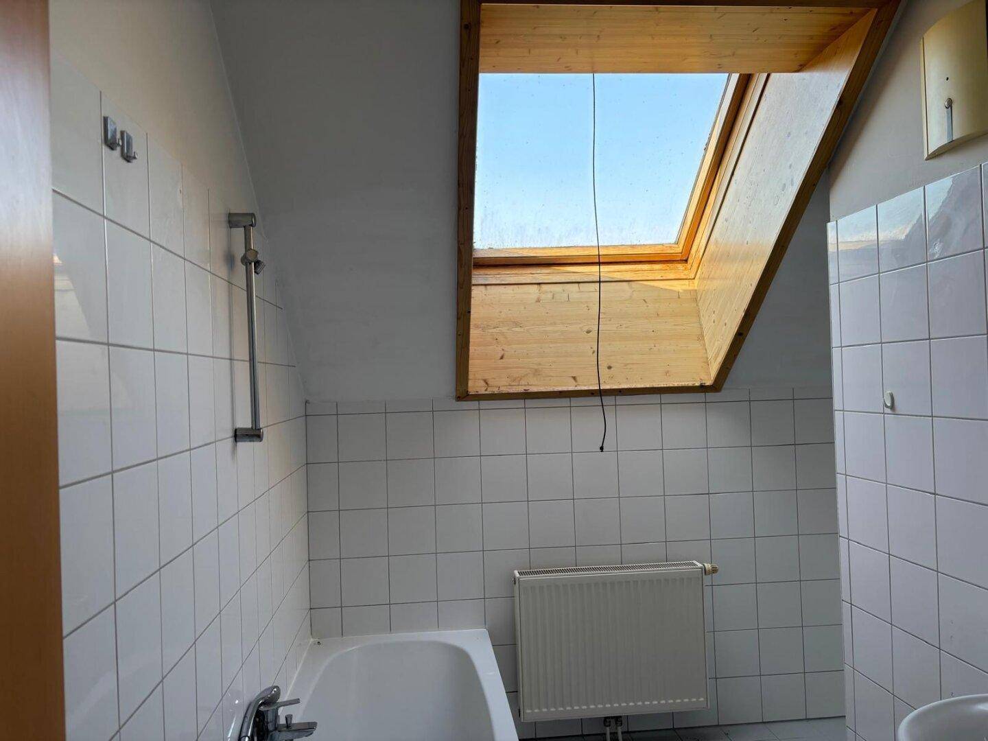 Badezimmer im Dachgeschoss mit Badewanne, weißen Fliesen und einem Dachfenster.