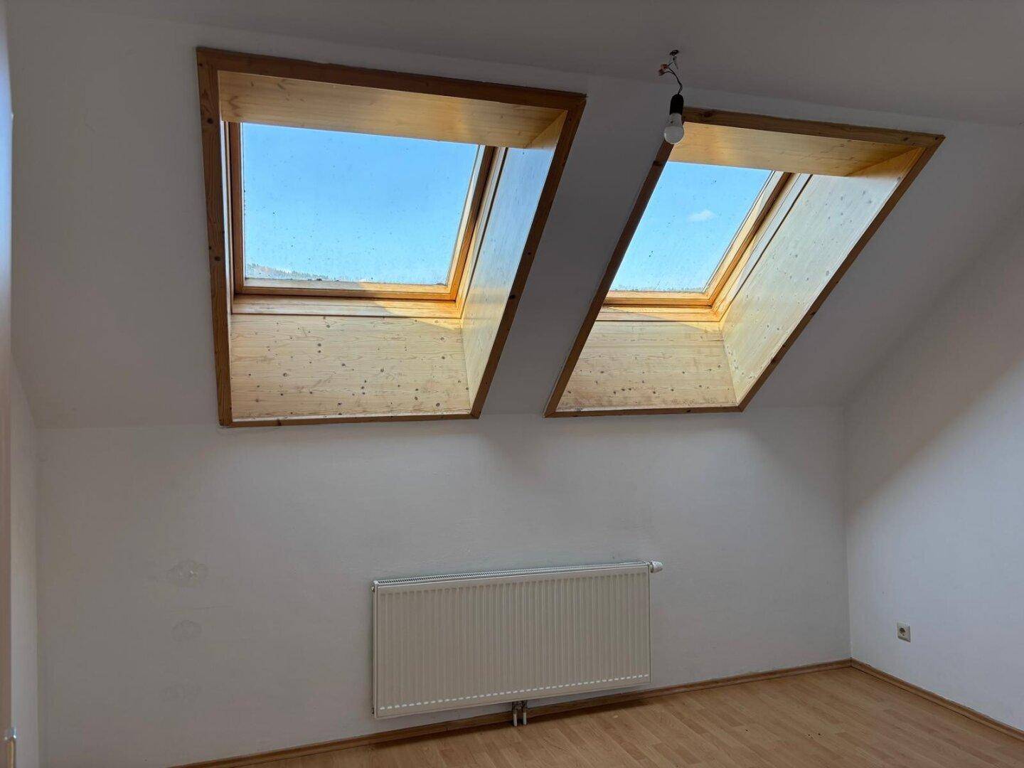 Dachgeschossraum mit zwei großen Dachfenstern, die viel Tageslicht hereinlassen.