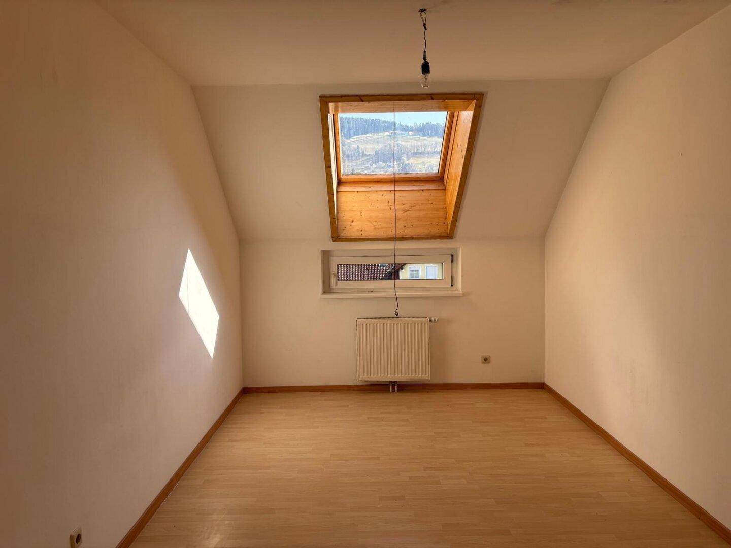 Heller Dachgeschossraum mit Holzboden, schrägen Wänden und einem großen Dachfenster.