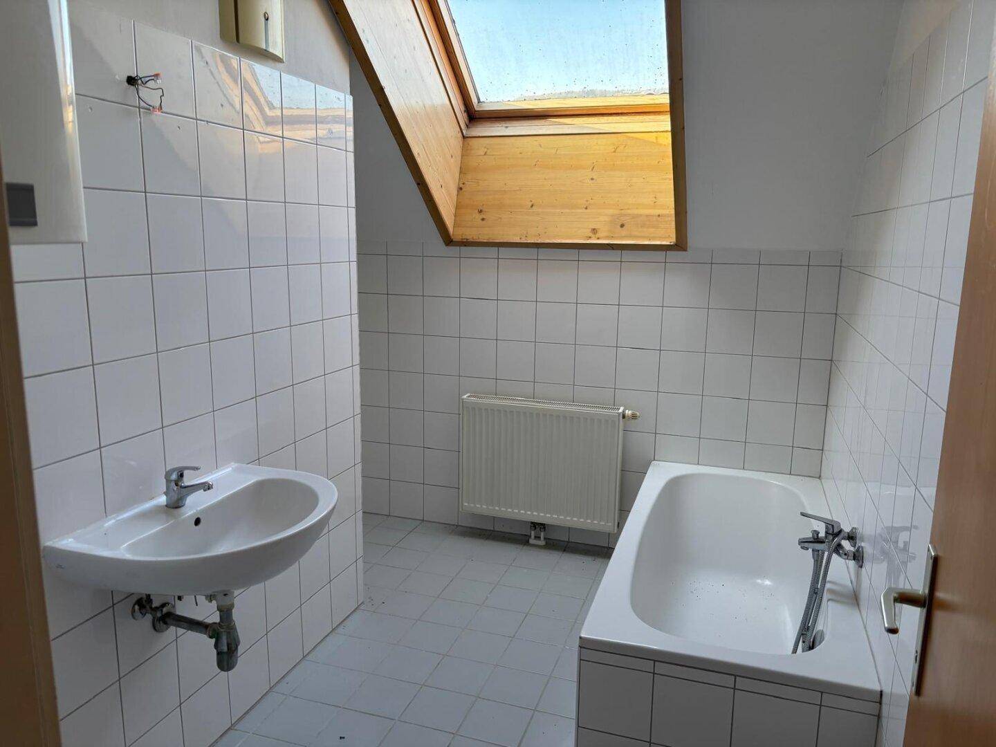 Gefliestes Badezimmer mit Badewanne, Waschbecken, Heizkörper und einem Dachfenster für Tageslicht.