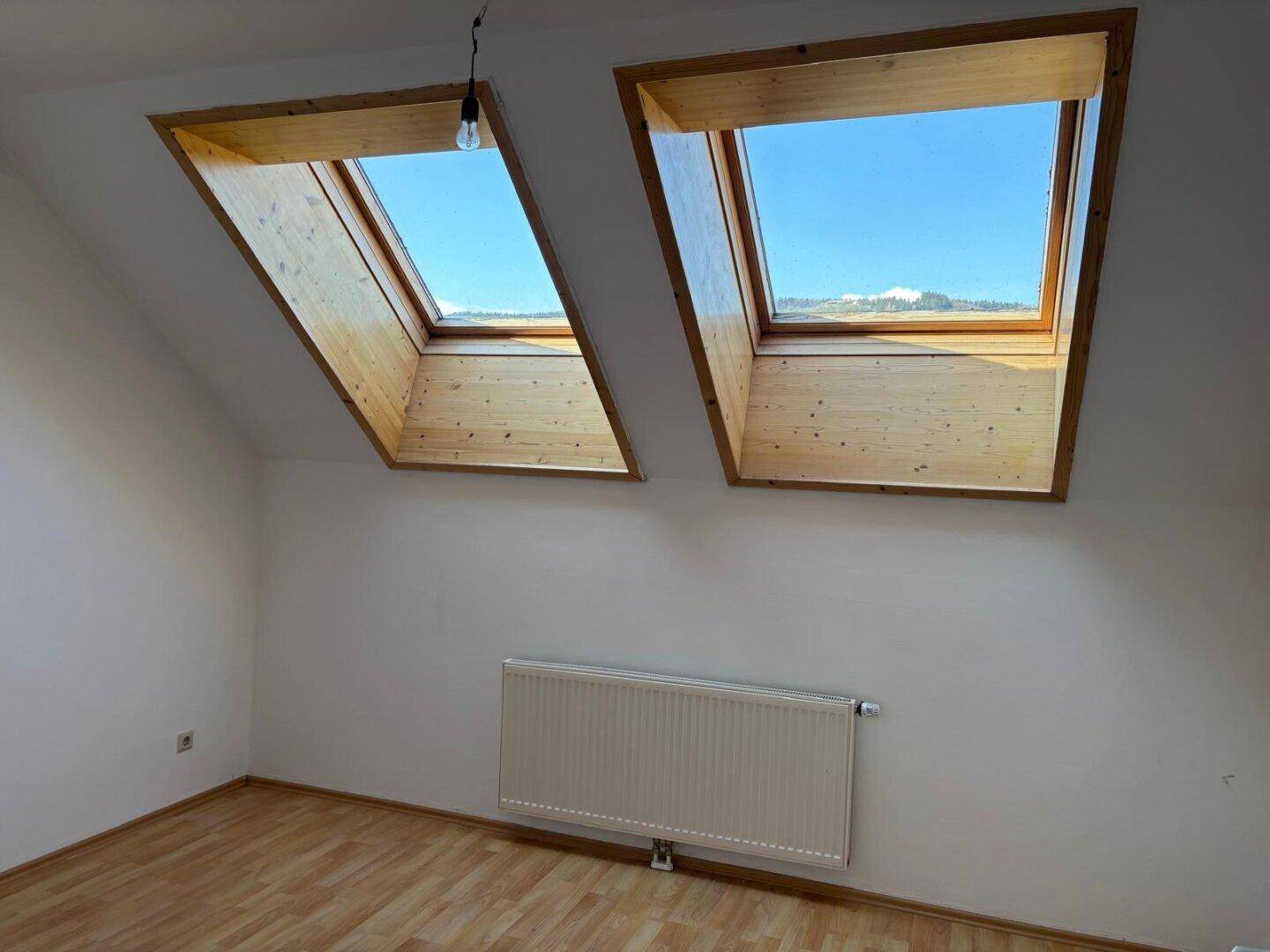 Helles Zimmer mit Laminatboden, weißen Wänden und zwei großen Dachfenstern für optimale Belichtung.