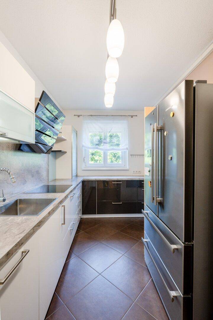 Moderne Küche mit weißen und dunklen Schränken, Edelstahlgeräten und Fliesenboden.