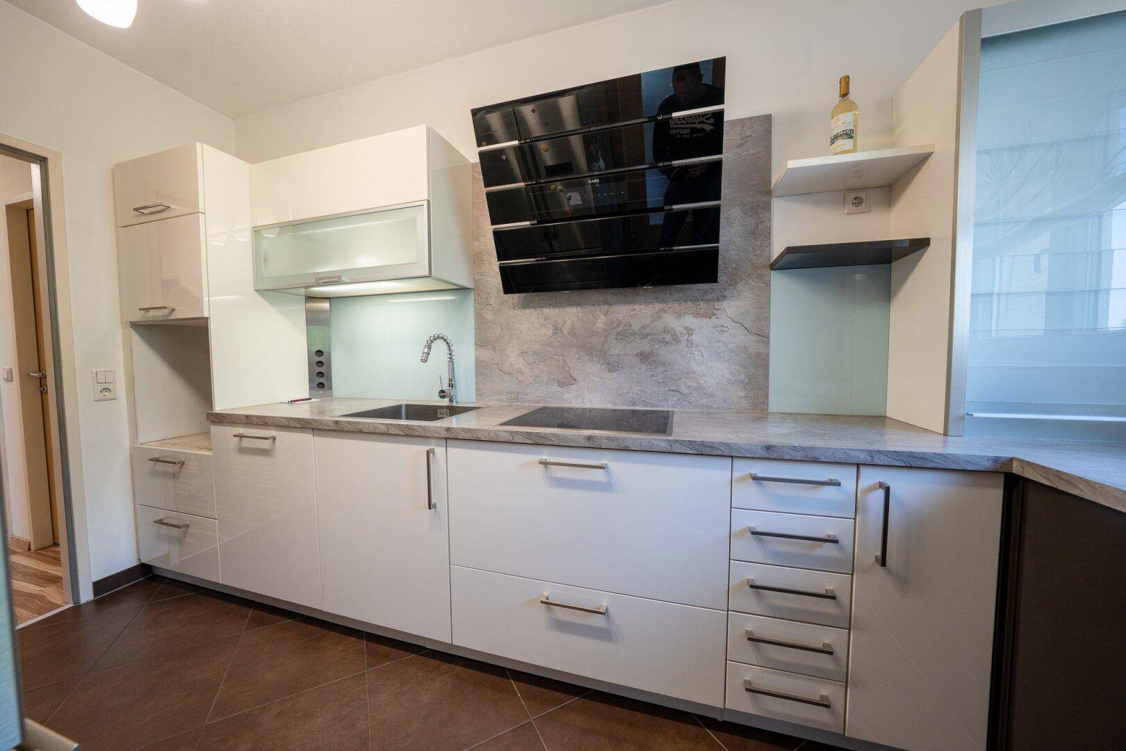 Moderne Einbauküche mit weißen Hochglanzfronten, dunkler Arbeitsplatte und Dunstabzugshaube.