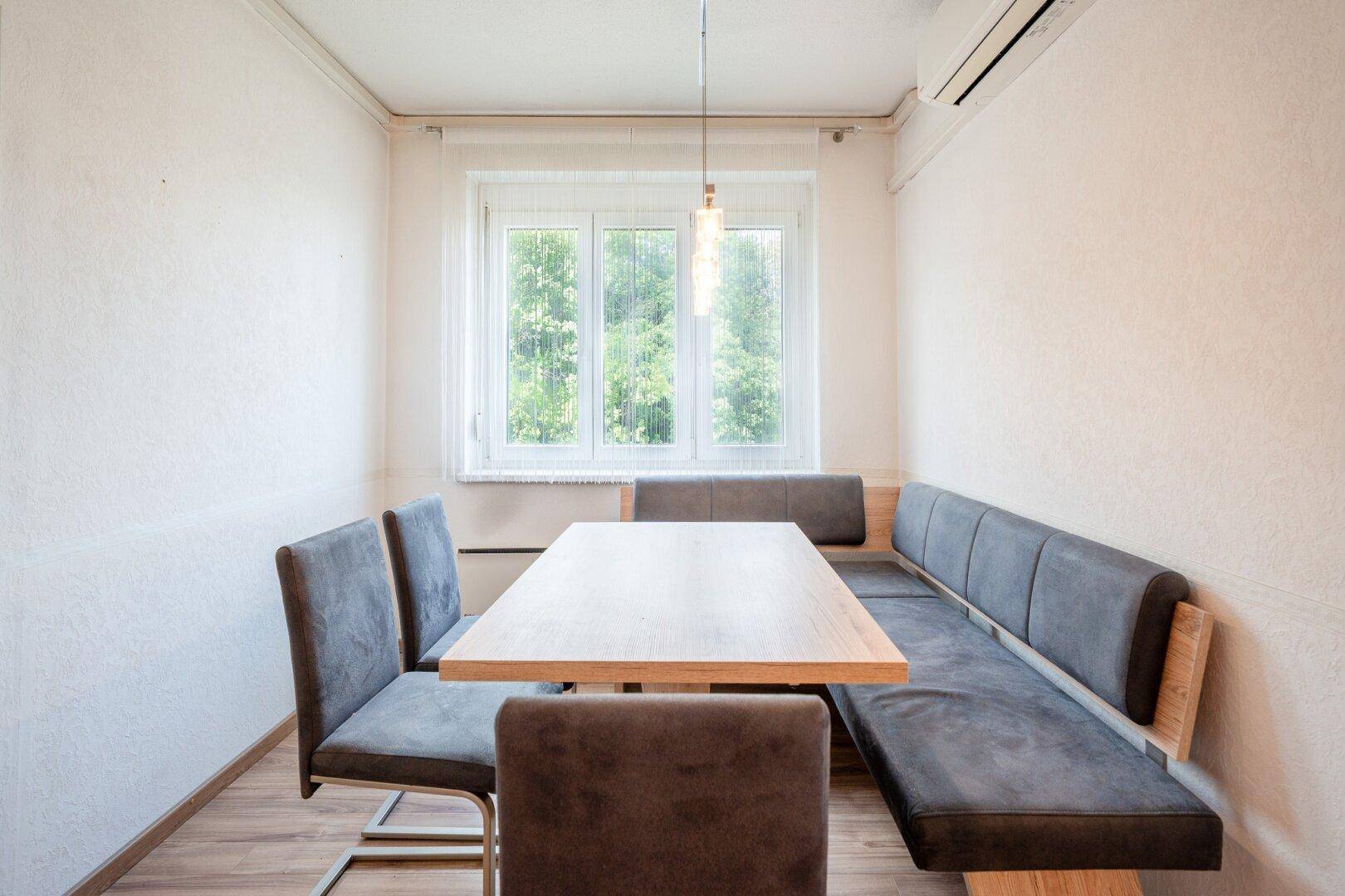 Gemütlicher Essbereich mit Holztisch, Sitzbank und Fenster mit Blick ins Grüne.