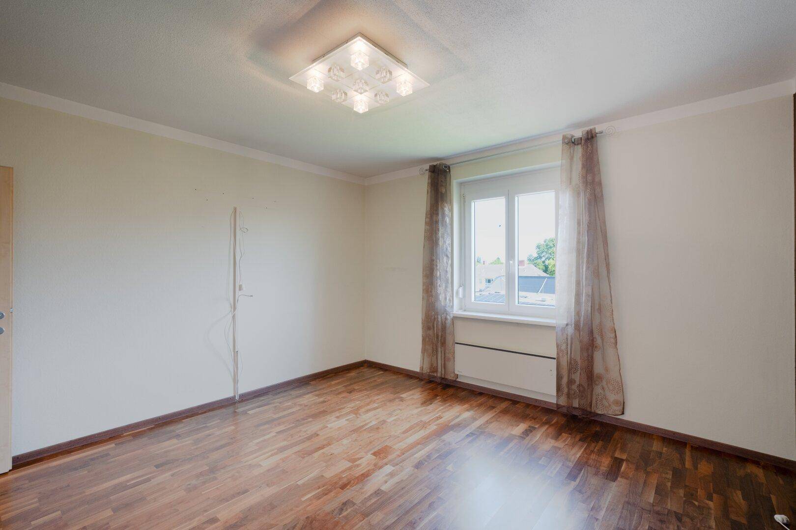 Geräumiges Schlafzimmer mit Holzboden, großen Fenstern und neutralen Wänden.