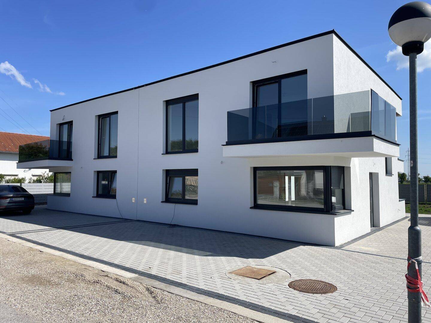 Moderne Doppelhaushälfte mit weißer Fassade, schwarzen Fenstern und Glasbalkonen.