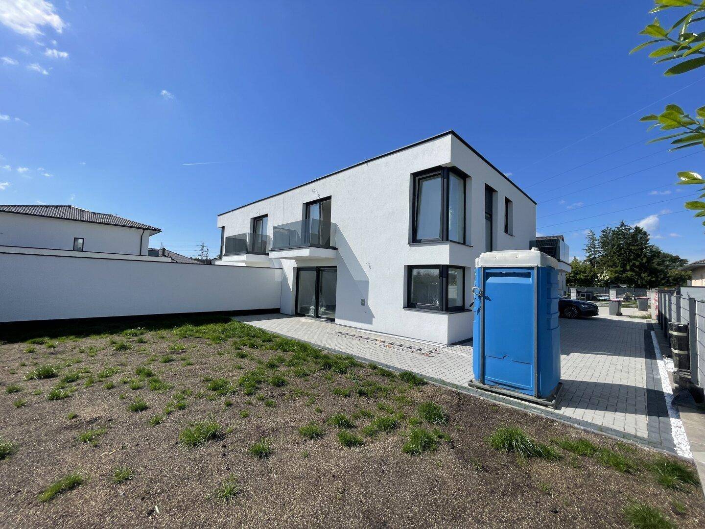 Hinteransicht der Doppelhaushälfte mit unfertigem Gartenbereich und gepflasterter Terrasse.