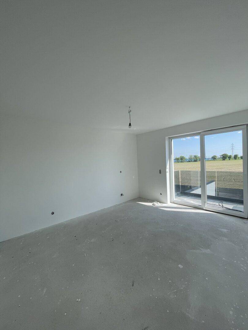 Geräumiger, unfertiger Wohnraum mit großen Fenstern und Blick auf die Felder.