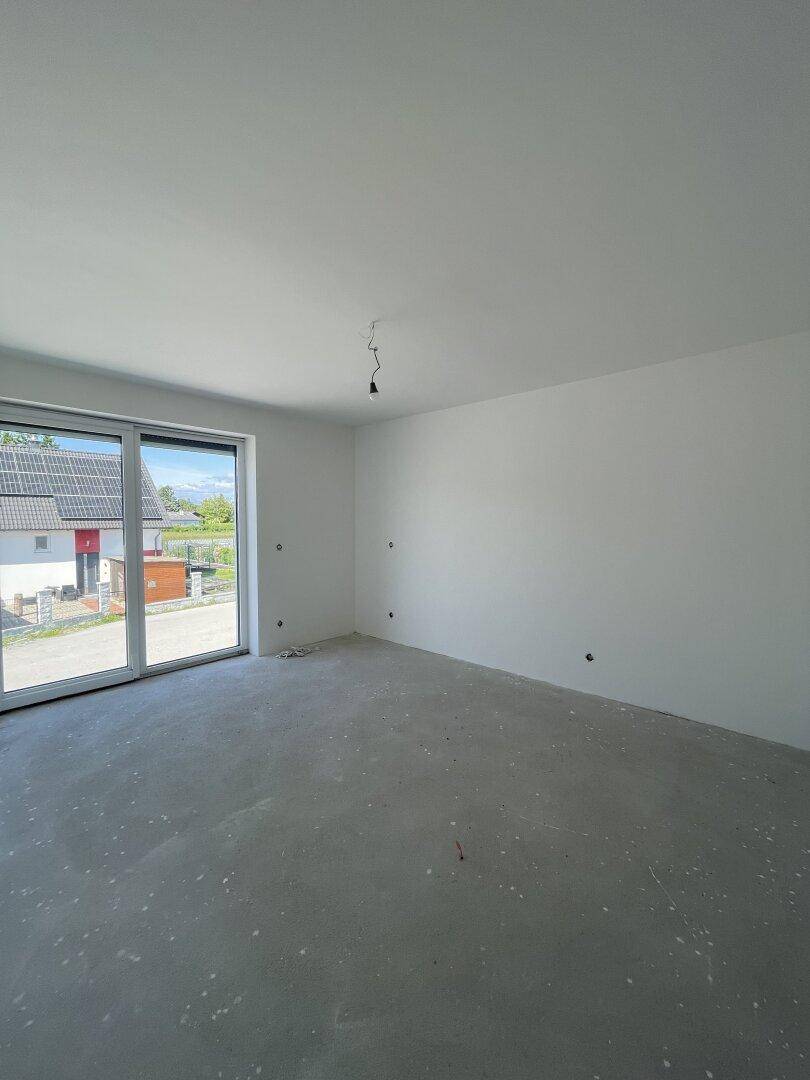 Heller, unfertiger Wohnraum mit großen Fenstern und Blick auf die Nachbarschaft.