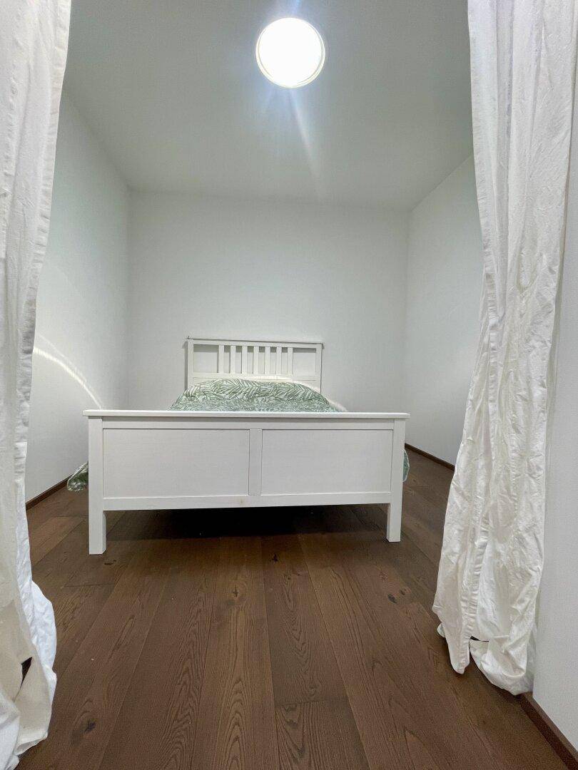 Helles Schlafzimmer mit weißem Bett, Holzboden und einem runden Oberlicht für natürliches Licht.