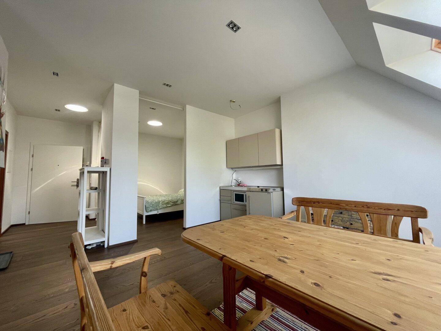 Offener Wohn- und Essbereich mit integrierter Küchenzeile und Zugang zu einem weiteren Zimmer.