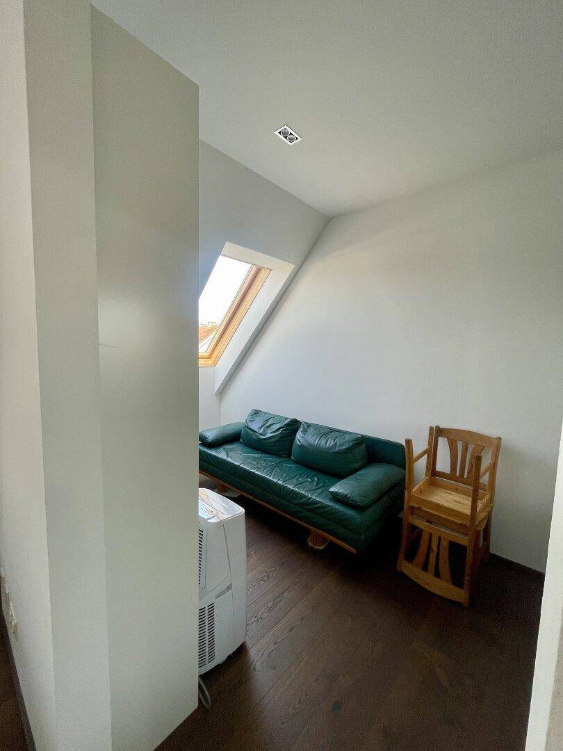 Gemütlicher Wohnbereich mit grünem Sofa, Holzboden, Dachschräge und einem Dachfenster.