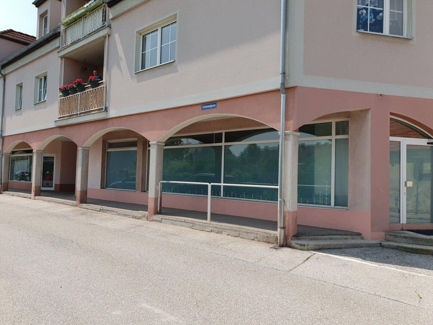Detailansicht des Eckgebäudes mit großen Schaufenstern im Erdgeschoss und einem Balkon im Obergeschoss.