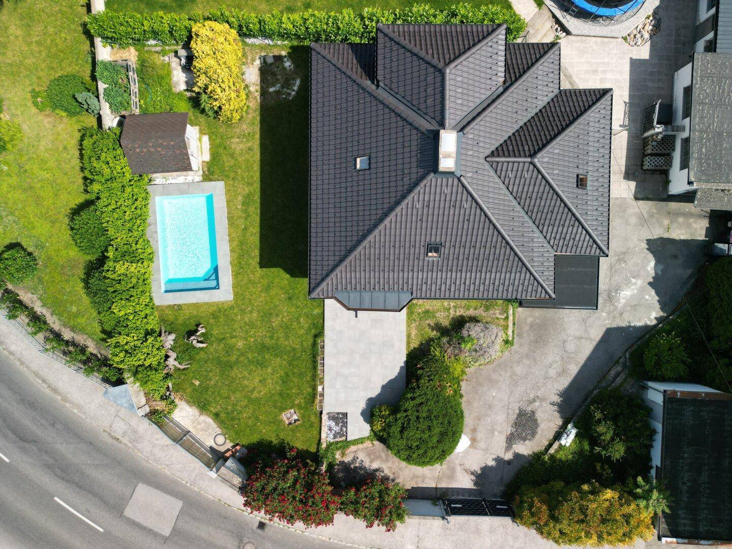 Vogelperspektive des Hauses mit dunklem Ziegeldach, Garten, Pool und angrenzender Straße.