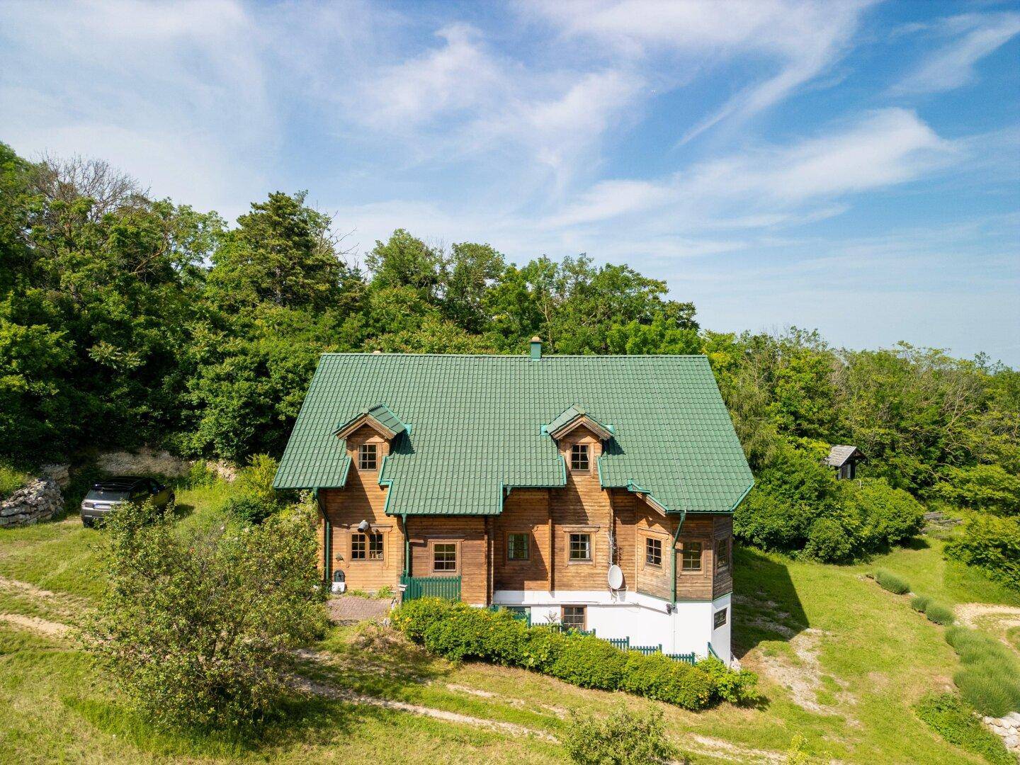 Charmantes Holzhaus mit grünem Dach und gepflegter Hecke, eingebettet in die natürliche Hügellandschaft.