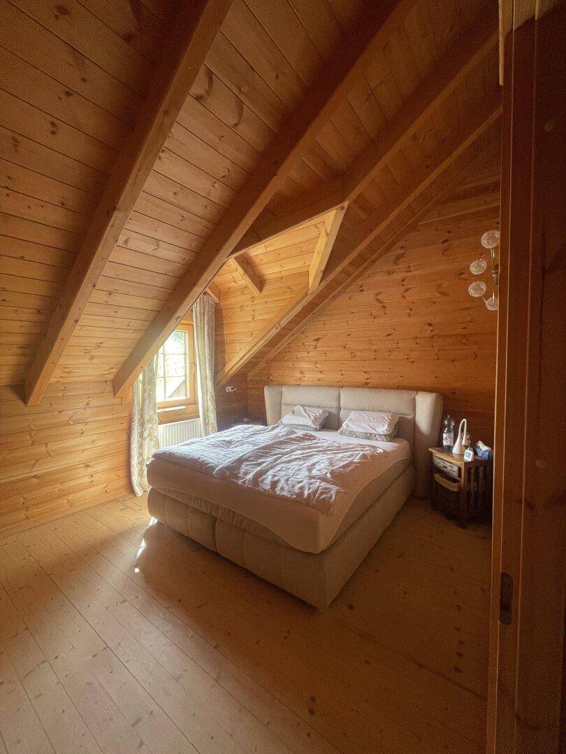 Gemütliches Schlafzimmer mit Holzwänden, Dachschräge und einem großen Bett, hell durch das Fenster.