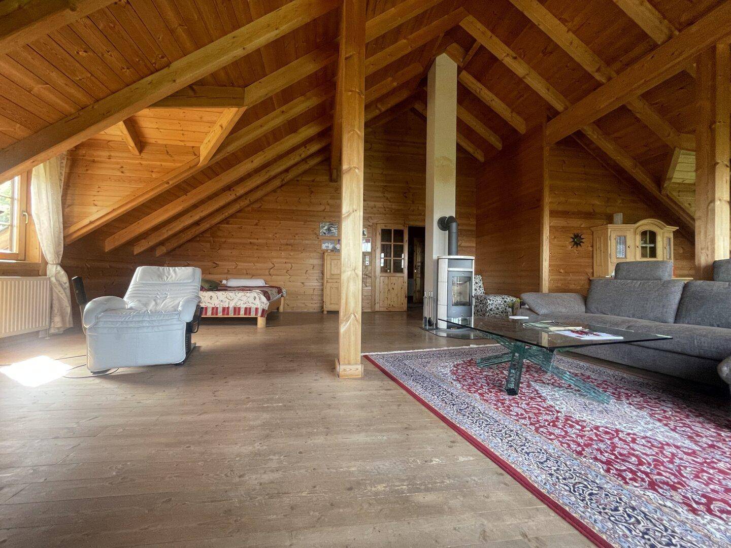 Großer offener Dachbodenbereich mit sichtbaren Holzbalken, als Wohnraum genutzt mit Sofa und Kaminofen.