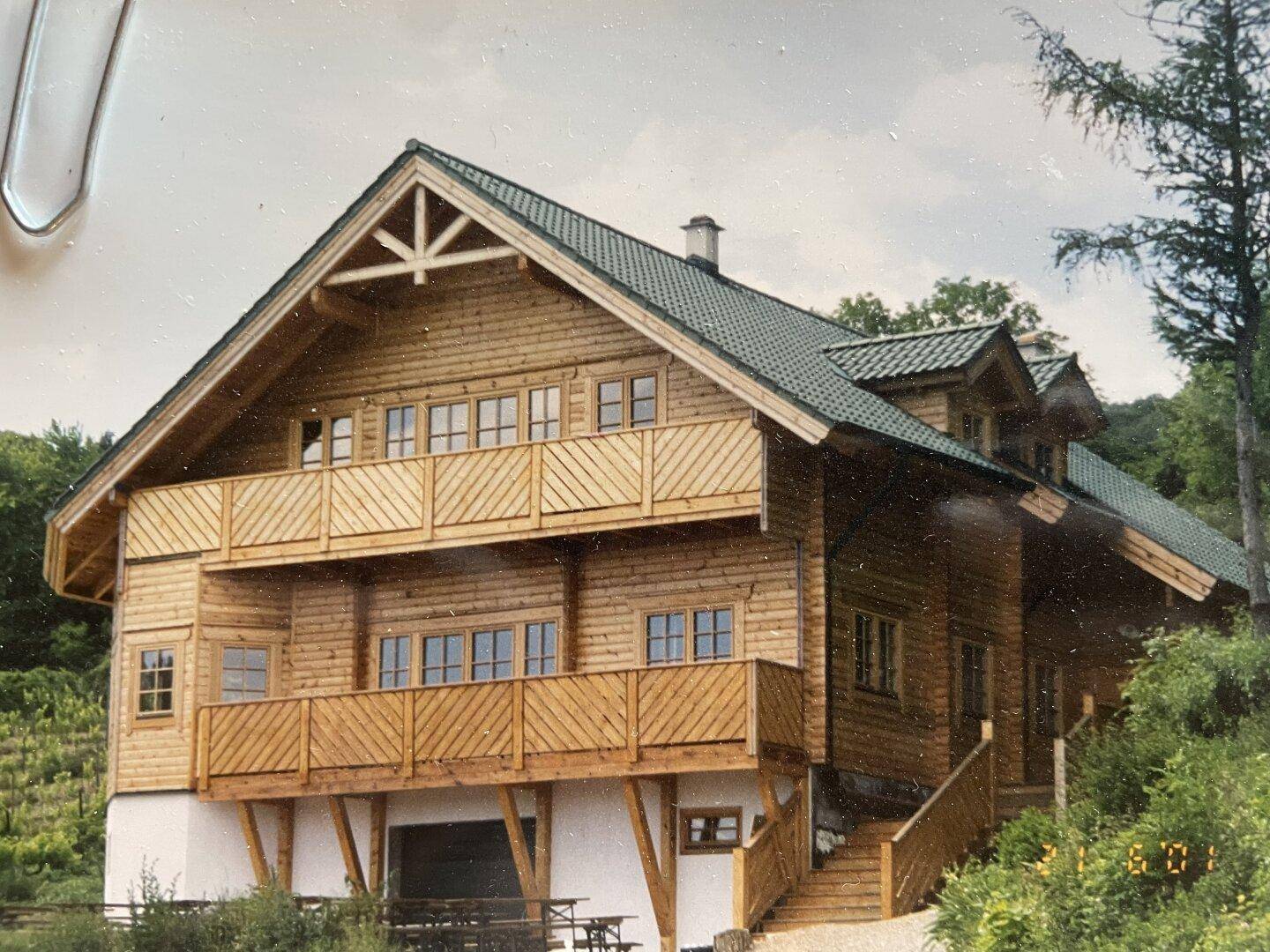 Älteres Foto des Holzhauses in neuwertigem Zustand mit hellerer Holzfassade und Balkonen.